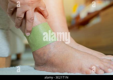 Side view close-up of senior woman's hand using green patch for relieve pain and relax on foot. Injury feet and ankle concept. Stock Photo