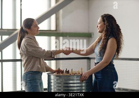 Young Adult Women Shaking Hands after Playing Chess Indoors Stock Photo