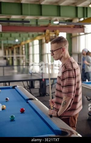 Vertical of Young Man Playing Billiards in Industrial Style Recreation Center Stock Photo