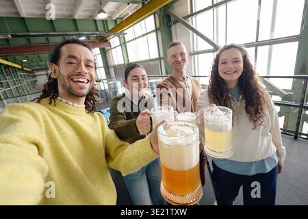 Multiethnic Young Adults Toasting Beer Glasses and Smiling at Brewery Gathering Stock Photo