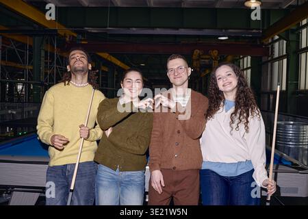Diverse Young Adults Smiling and Gesturing Heart Shape While Playing Billiards Stock Photo