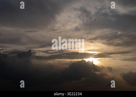 Dramatic sky with dark clouds and golden sunbeam piercing through. Sunlight glows softly behind heavy, textured clouds. Silhouetted storm clouds frame Stock Photo