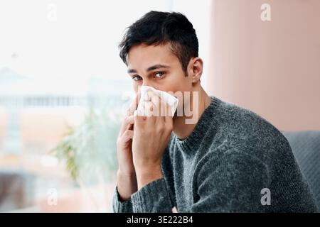 Sick, man and portrait with tissue in home for blowing nose, influenza or virus infection on sofa. Male person, hayfever or sinus with allergy, cold Stock Photo