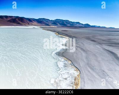 Aerial view of a saline lake shoreline in the Argentine Puna desert with mountains in the background, Argentina. Stock Photo