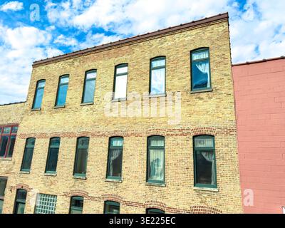 A structure made of brick stands tall with several windows on its facade. The blue sky has light clouds and the sun shines on the building in the city Stock Photo