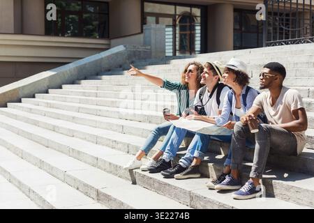 Multiethnic tourists sitting on stairs with map Stock Photo