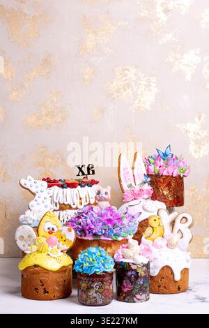 Luxurious collection of hand-decorated Easter kulichi with colorful icings, fondant figures. Spring holiday composition on golden-beige background, pe Stock Photo