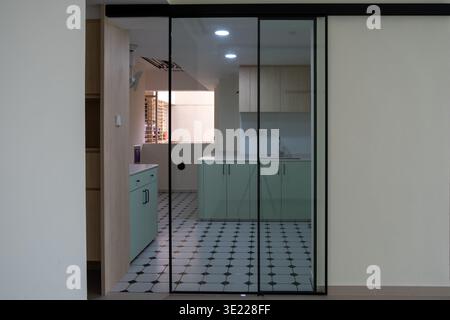 Minimalist kitchen viewed through glass sliding doors. Light green cabinets contrast with dark frames. Black-framed doors divide living spaces elegant Stock Photo
