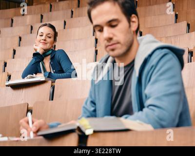 Two students in a lecture hall with notebooks, sitting among rows of wooden seats. Germany Stock Photo