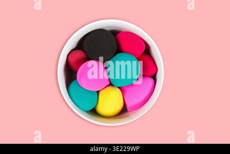 Bright colorful makeup sponges in a white bowl on a pink background. Stock Photo
