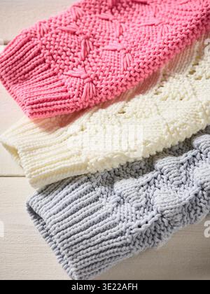 Stacked knitted sweaters in pink, cream, and gray patterns on a light wooden surface. Germany Stock Photo