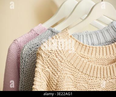 Three knitted sweaters in pastel colors hang on white hangers. Germany Stock Photo