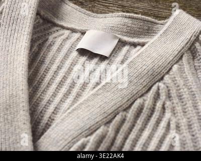 Close-up of a beige knitted sweater with a blank label on wooden background. Germany Stock Photo
