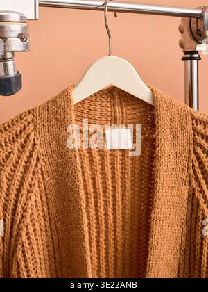 Brown knitted cardigan on a white hanger against a peach background. Germany Stock Photo