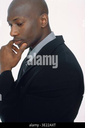 A man in a suit looks thoughtful while touching his chin against a plain background. Germany Stock Photo