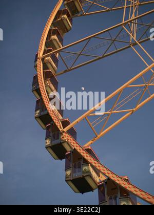 A section of a ferris wheel against a clear blue sky with the moon visible in daylight. Brussels, Belgium Stock Photo