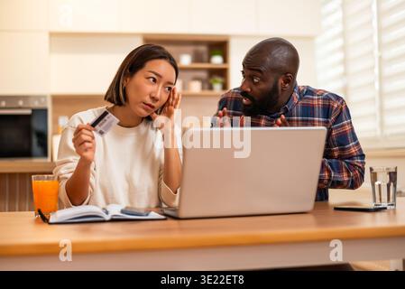 Concerned couple sits at a table and shopping online. Woman is holding a credit and man is talking to her. Stock Photo