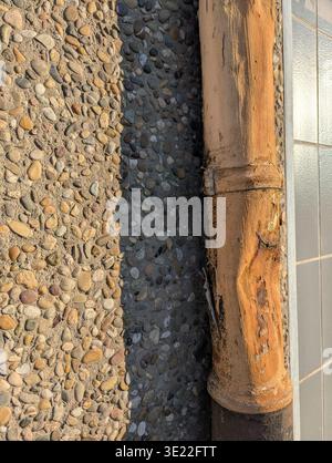 Rusted Downspout On Pebble Pavement, Tiled Edge And Shadow, Closeup Showing Corroded Metal Pipe Resting Against Textured Aggregate Ground And Glazed T Stock Photo