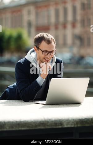 Male programmer or web designer freelancer read email on laptop computer outdoors walking city using mobile 5g internet connection. Freelance businessman travel and work online remotely on vacation || Model released Stock Photo