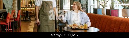 Young Woman Paying Restaurant Bill Using Contactless Card Reader Stock Photo