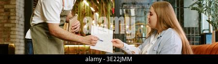 Young Woman Receiving Menu from Waiter While Sitting in Restaurant Stock Photo