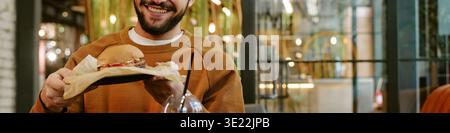 Young Adult Man Smiling While Holding Burger in Modern Restaurant Stock Photo