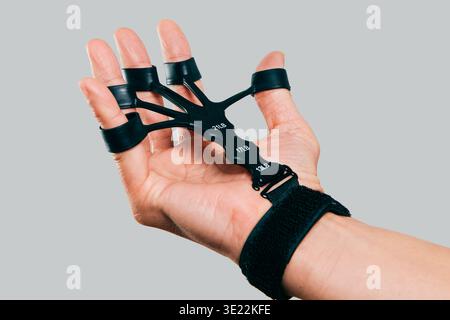 close view of a man using a hand grip trainer with finger loops and resistance levels labeled 13LB, 17LB and 21LB, strengthening fingers and forearm m Stock Photo