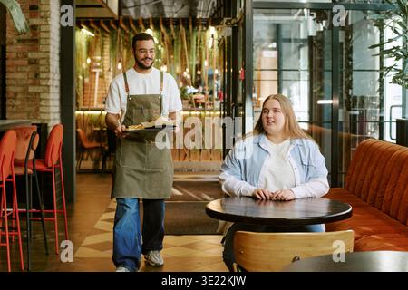 Young Woman Waiting While Young Man Serving Food in Modern Cafe Stock Photo