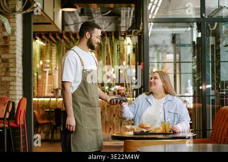 Young Woman Paying Bill to Middle Aged Man Waiter in Cafe Stock Photo