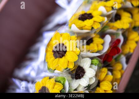 A beautiful cheerful yellow artificial sunflower craft made of crochet yarn flower resting on soft white satin fabric bringing warm nostalgic feeling Stock Photo
