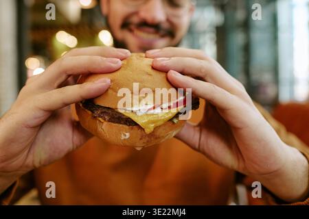 Young Adult Man Smiling While Holding Cheeseburger with Both Hands Stock Photo