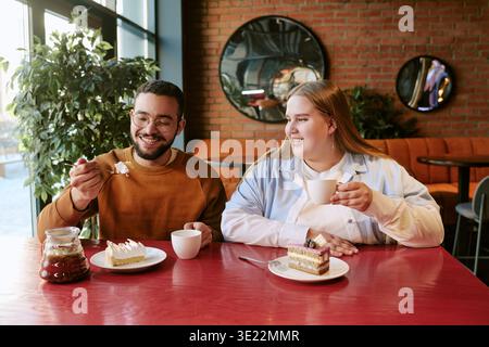 Young Woman and Young Man Smiling While Enjoying Cake at Cafe Stock Photo