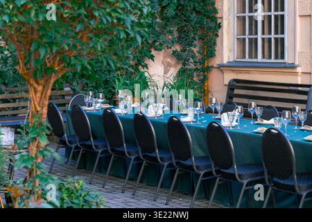 A long table is beautifully set with glassware, plates, and napkins in a charming outdoor courtyard setting Stock Photo