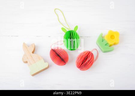 Colorful Easter decorative honeycomb eggs, wooden Easter bunny and candle flower on white wooden table. Happy Easter concept, greeting card. Top view Stock Photo