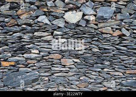 Texture of an old dry stone wall made of flat grey slates. Rustic stone wall background with various shapes and sizes of rocks. Stock Photo
