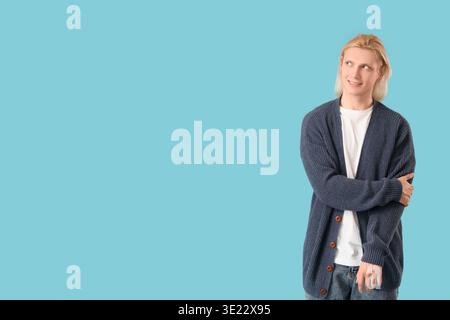 Young blonde man in cardigan on blue background Stock Photo