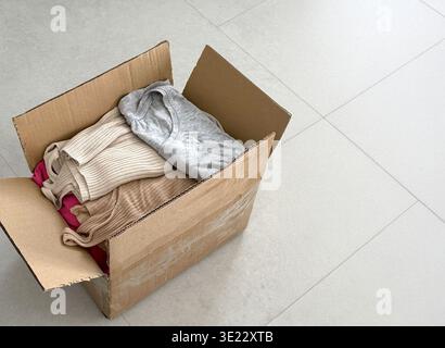 Cardboard box filled with neatly folded clothing items including sweaters and t-shirts placed  Stock Photo