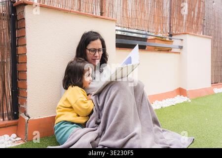 mother and daughter reading book together outdoors in terrace, parenting and motherhood Stock Photo