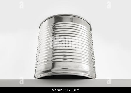 Close-up studio image of an empty ribbed metal tin can placed on a light minimal background. The shot emphasizes the reflective metallic surface and c Stock Photo