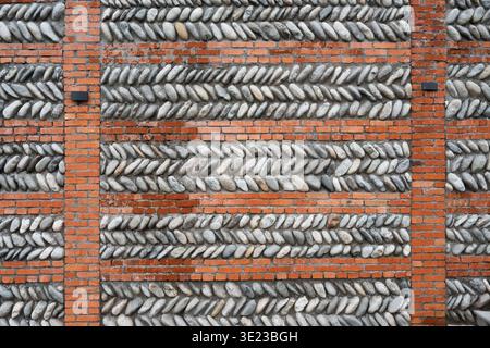 Unique wall texture combining red bricks and grey river stones in a herringbone pattern. Decorative masonry wall with horizontal brick rows and diagon Stock Photo