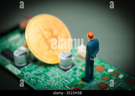 Miniature businessman standing on circuit board facing bitcoin coin, symbolizing digital finance, cryptocurrency and future economy Stock Photo