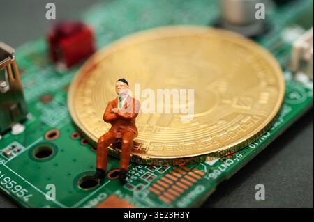 Miniature businessman sitting on bitcoin on circuit board, representing digital currency, fintech investment and modern economy concept Stock Photo