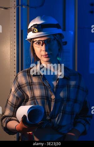 Electrical engineer holding system blueprint near industrial switchboard. Engineering portrait. Stock Photo