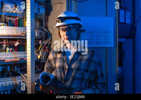 Female electrical engineer standing near switchboard holding technical blueprint. Energy engineering Stock Photo