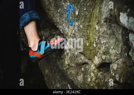 Fontainebleau, France - April 22, 2019: A close-up of a climber's foot in a bicolour (blue/red) climbing shoe, bouldering on a massive sandstone rock. Stock Photo