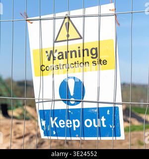 Warning construction site, keep out sign, fixed to metal fencing in front of a childrens playground under development. Stock Photo