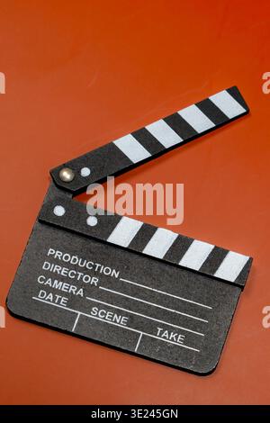 A classic clapperboard sits on a contrasting orange surface, ready for the next scene to be filmed. Stock Photo