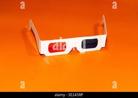A pair of cyan red cardboard 3D glasses on orange background.  Stock Photo