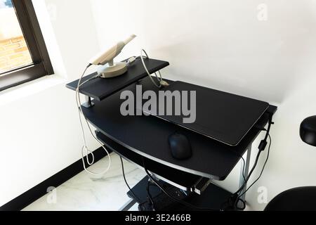 High-angle view of a modern minimalist office workstation. A closed black laptop, computer mouse, and white router sit on a clean, black ergonomic des Stock Photo