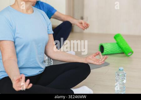 Yoga mindfulness meditation. Senior mature couple practicing yoga at home. Hands in chin mudra gesture. Old husband wife sitting in lotus pose meditating relaxing. Family doing breathing practice. Stock Photo